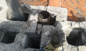 Czyszczenie komina z kwasówki. Widoczna szczotka kominiarska i fragmenty dachu.