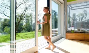 Kobieta w letniej sukience otwiera drzwi, wychodząc na taras. Duże okna wpuszczają mnóstwo światła do nowoczesnego wnętrza.