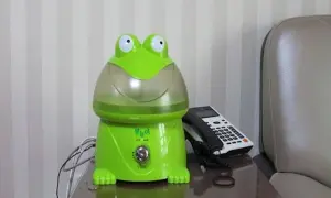 Zielony nawilżacz powietrza dla niemowlaka w kształcie żaby, obok telefonu.
