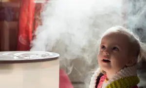 Dziecko z zaciekawieniem patrzy na parę z nawilżacza, który pomaga zwalczyć suche powietrze i kaszel.