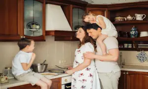 Rodzina w kuchni przygotowuje naleśniki. Tata niesie córkę na barana, mama miesza ciasto, a synek siedzi na blacie. LZO co to? To rodzinne chwile!