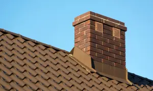Solidna ceramika kominowa z brązowej cegły, wznosząca się ponad brązowym dachem pod błękitnym niebem.