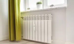Biały grzejnik pod oknem z zieloną zasłoną. Dowiedz się, jak nawilżyć powietrze w pokoju zimą, by uniknąć suchego klimatu.