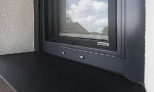 Szczelne uszczelnienie parapetu zewnętrznego okna DAKO. Ciemny parapet i szara rama okna zapewniają estetykę i ochronę.