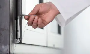 Dłoń z kluczem imbusowym wykonuje regulację okna balkonowego, precyzyjnie dostosowując zawias.