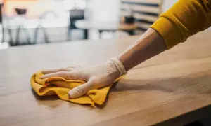 Ręka w rękawiczce ściera kurz na meblach żółtą ściereczką.