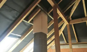 Kratownica pod komin z betonu i drewna, otoczona czarną membraną dachową, w trakcie budowy poddasza.