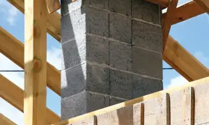 Solidny fundament pod komin systemowy, wznoszony z bloczków betonowych, otoczony drewnianą konstrukcją dachu.