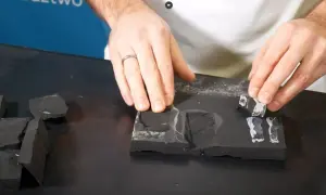 Dłonie układają fragmenty czarnego materiału, przypominającego fartuch EPDM, na ciemnej powierzchni. Montaż wymaga precyzji.