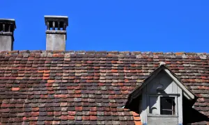 Dwa kominy na dachu pokrytym starymi dachówkami, wymagające naprawy komina z cegły.