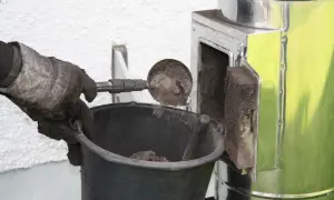 Rękawica z miarką wysypuje sadzę do wiadra. To prosty sposób, jak wyczyścić komin bez wchodzenia na dach.