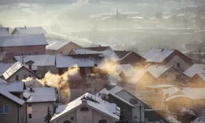 Zimowy poranek we mgle, z domów unosi się dym, co wpływa na jakość powietrza.