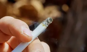 Dłoń trzymająca zapalonego papierosa, z którego unosi się dym. Zastanawiasz się, jak usunąć zapach papierosów ze ścian?
