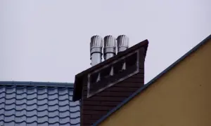 Trzy nasady kominowe na ceglanym kominie, świadczące o prawidłowym montażu nasady kominowej. Obok dach z niebieską dachówką.