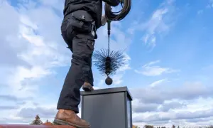 Kominiarz na dachu z narzędziami. Czy można czyścić komin jak się pali w piecu? Nie, to niebezpieczne.