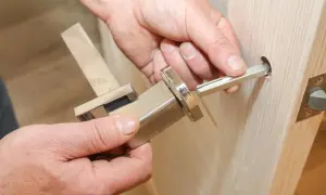 Dłoń wyciąga metalowy trzpień z klamki okiennej, pokazując jak wyjąć trzpień z klamki okiennej.