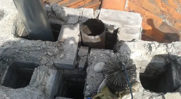Czyszczenie komina z kwasówki. Widoczna szczotka kominiarska i fragmenty dachu.