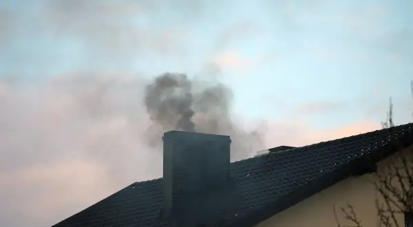 Ciemny dym wydobywa się z zimnego komina na tle błękitnego nieba z chmurami.