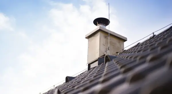 Nowy komin w starym domu, na który uzyskano pozwolenie, dumnie wznosi się na tle błękitnego nieba.