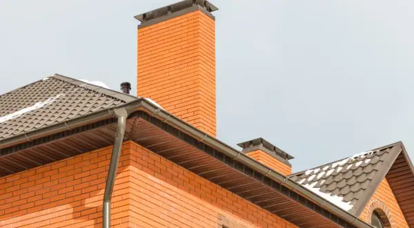 Eleganckie zakończenie komina systemowego z cegły, zwieńczone metalową nakładką, chroni przed warunkami atmosferycznymi.