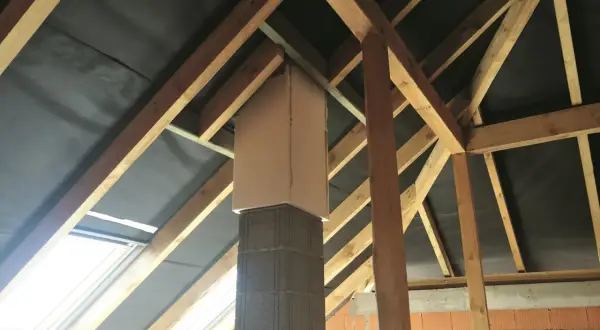 Kratownica pod komin z betonu i drewna, otoczona czarną membraną dachową, w trakcie budowy poddasza.