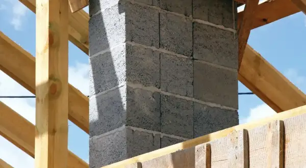 Solidny fundament pod komin systemowy, wznoszony z bloczków betonowych, otoczony drewnianą konstrukcją dachu.