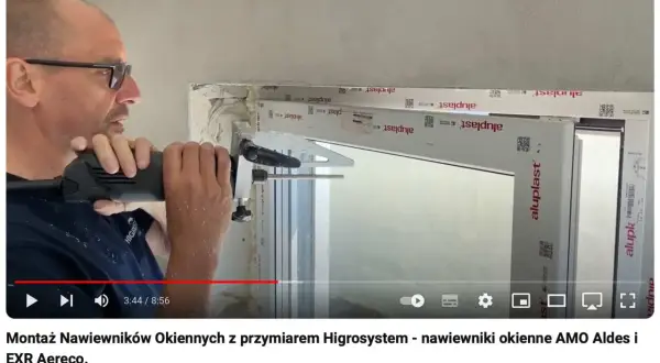 Montaż nawiewnika w oknie. Mężczyzna wierci otwór w ramie okiennej, przygotowując miejsce na nawiewnik.