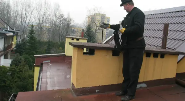 Kominiarz w cylindrze przygotowuje się do przeglądu kominiarskiego, trzymając w rękach liny.