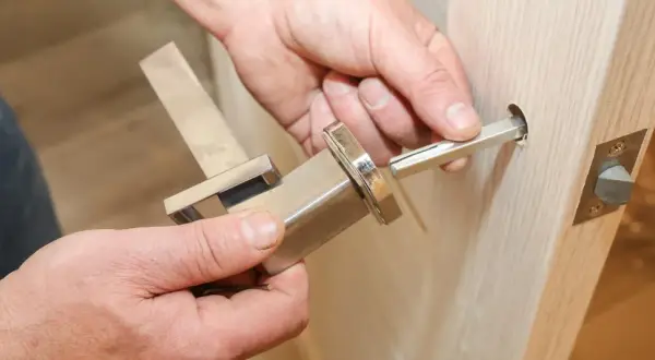 Dłoń wyciąga metalowy trzpień z klamki okiennej, pokazując jak wyjąć trzpień z klamki okiennej.