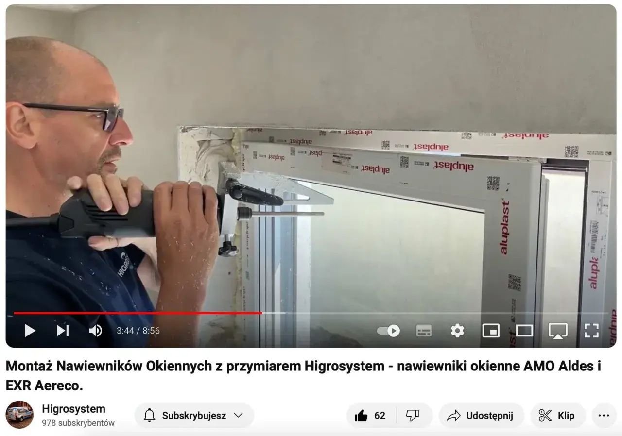 Montaż nawiewnika w oknie. Mężczyzna wierci otwór w ramie okiennej, przygotowując miejsce na nawiewnik.