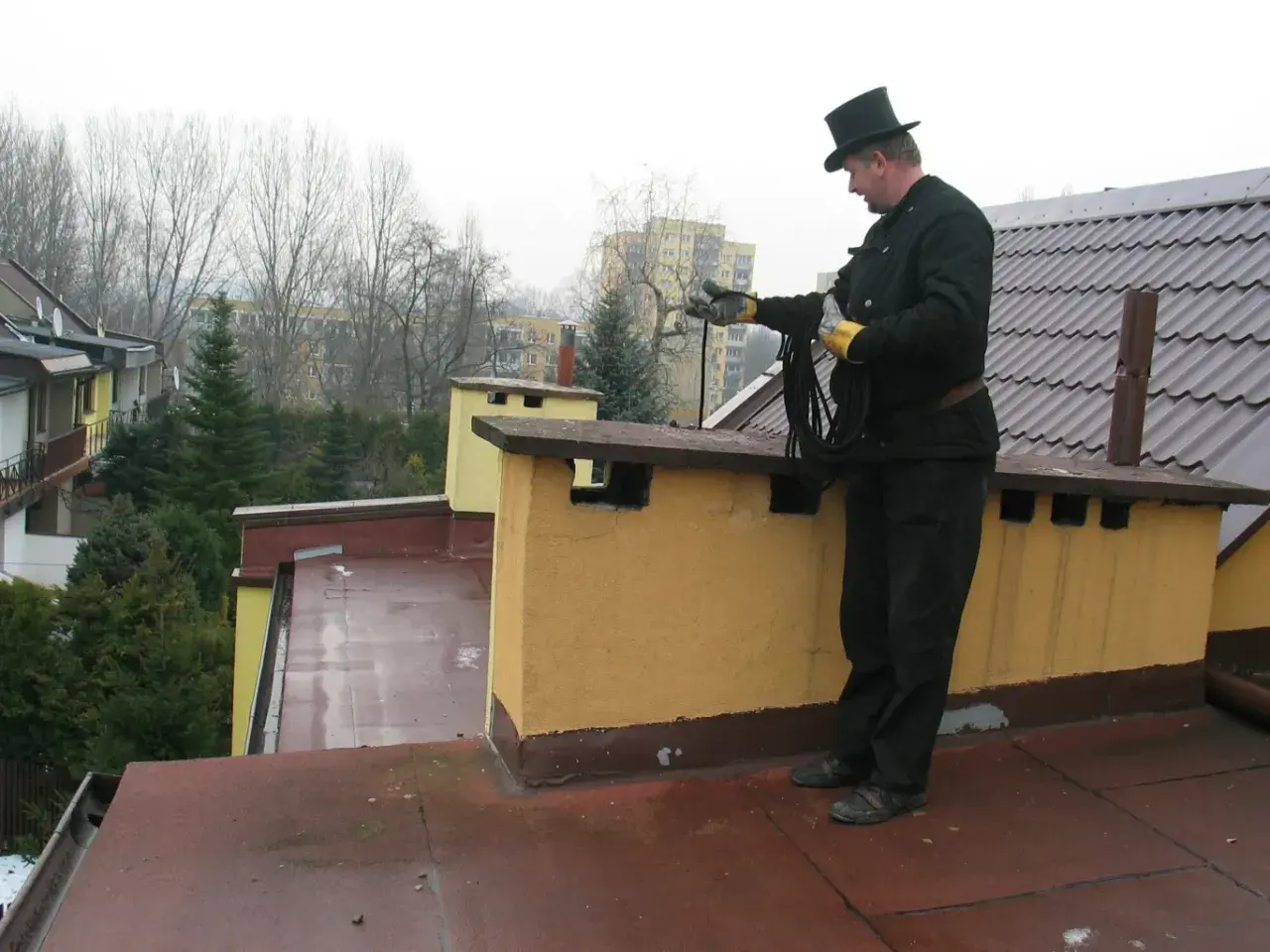Kominiarz w cylindrze przygotowuje się do przeglądu kominiarskiego, trzymając w rękach liny.