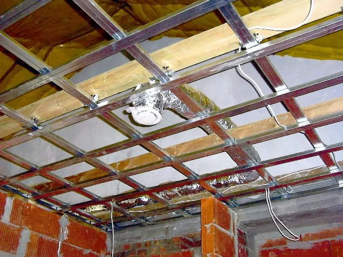 Konstrukcja sufitu podwieszanego z widoczną instalacją wentylacji grawitacyjnej w suficie. Widać metalowy stelaż, drewniane belki, izolację i przewód wentylacyjny.