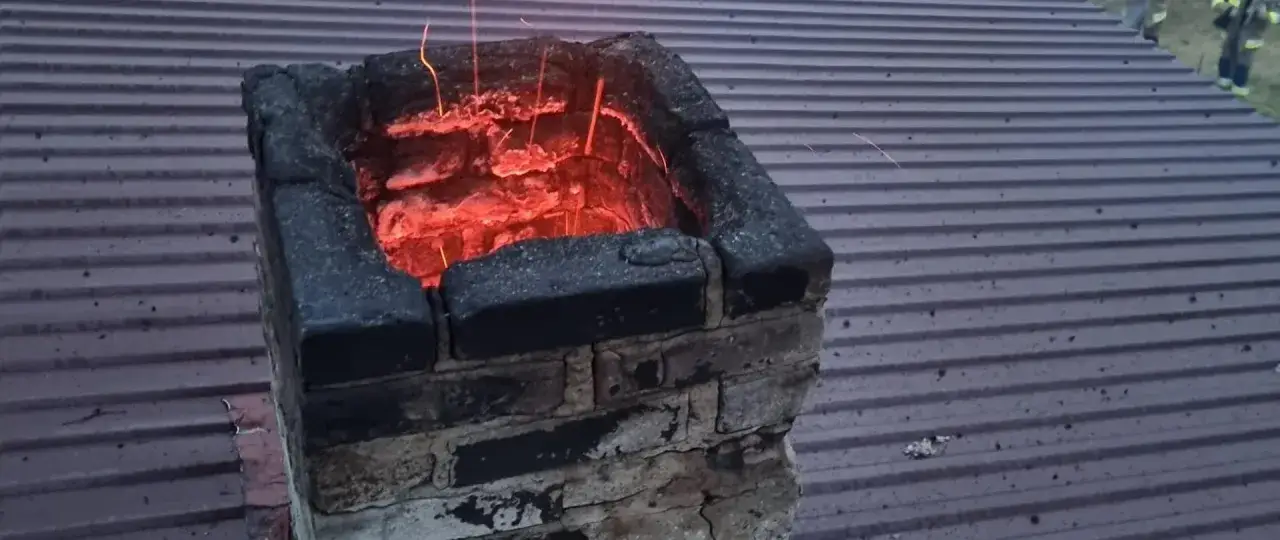 Żarzący się komin po nieudanym czyszczeniu komina obierkami z ziemniaków. Iskry unoszą się nad dachem.