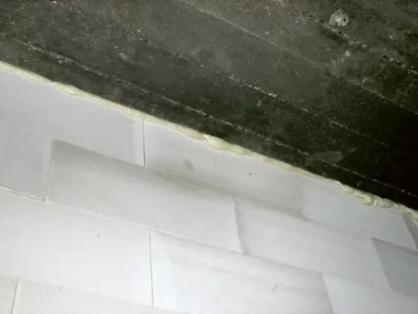 Dylatacja komina wykonana pianką montażową między betonowym stropem a białymi bloczkami.