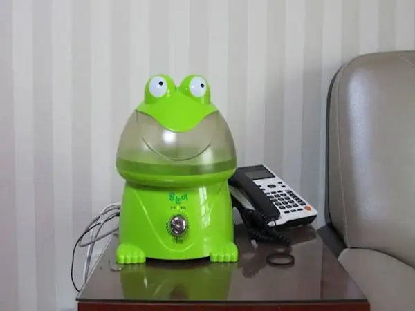 Zielony nawilżacz powietrza dla niemowlaka w kształcie żaby, obok telefonu.