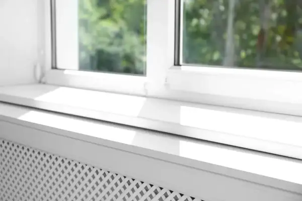 Biały parapet pod okno, z widocznym fragmentem grzejnika, odbija światło słoneczne.