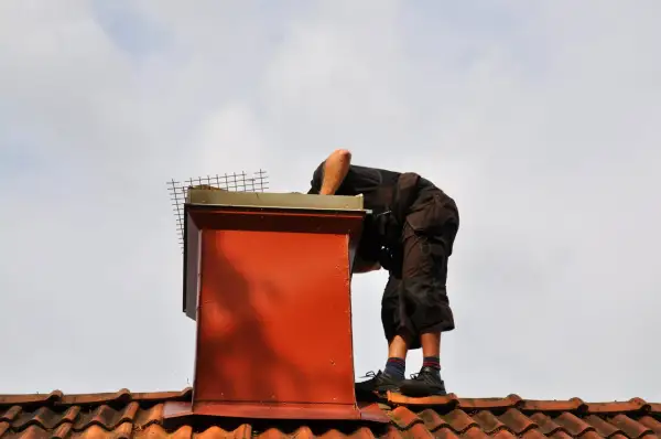 Pracownik na dachu wykonuje uszczelnianie komina, dbając o jego szczelność i bezpieczeństwo.