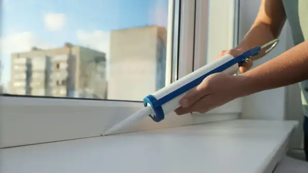 Uszczelnianie parapetu przy oknie za pomocą pistoletu z masą silikonową. Dowiedz się, jak zamknąć okno, by było szczelne.