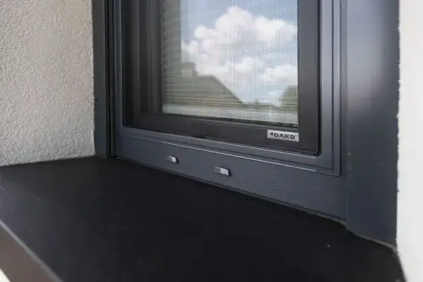 Szczelne uszczelnienie parapetu zewnętrznego okna DAKO. Ciemny parapet i szara rama okna zapewniają estetykę i ochronę.