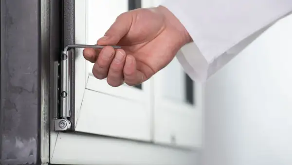 Dłoń z kluczem imbusowym wykonuje regulację okna balkonowego, precyzyjnie dostosowując zawias.
