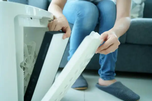 Osoba wyjmuje filtr z oczyszczacza powietrza. Czy filtr HEPA można myć wodą? Zależy od modelu, ten wygląda na jednorazowy.
