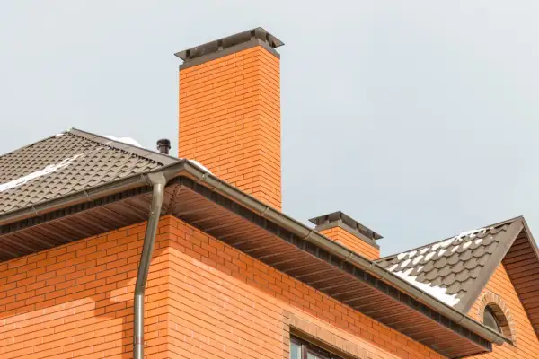 Eleganckie zakończenie komina systemowego z cegły, zwieńczone metalową nakładką, chroni przed warunkami atmosferycznymi.