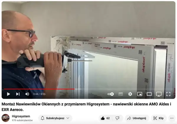 Montaż nawiewnika w oknie. Mężczyzna wierci otwór w ramie okiennej, przygotowując miejsce na nawiewnik.