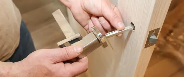 Dłoń wyciąga metalowy trzpień z klamki okiennej, pokazując jak wyjąć trzpień z klamki okiennej.